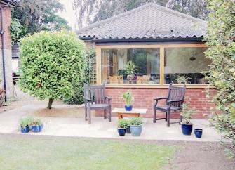 Exterior of a single storey Norfolk holiday lodge With a patio and lawn.