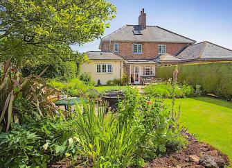 A brick house overlooks a large lawn with flower-filled borders