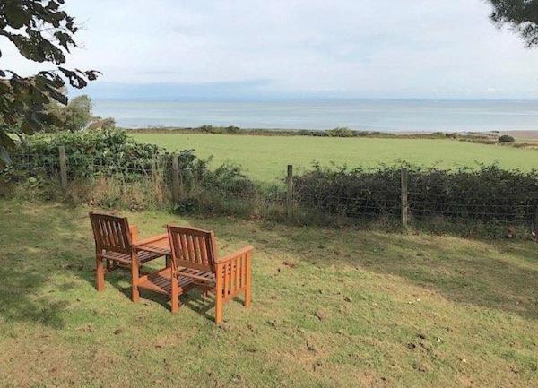 A pair of garden chairs face towards fields and the sea.