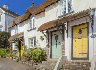 The exterior of a small terrace of thatched cottages overlooks a quiet North Devon village street.