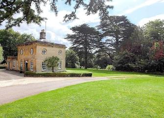 Exterior of a stone-built Cotswold country house surrounded by trees and parkland.