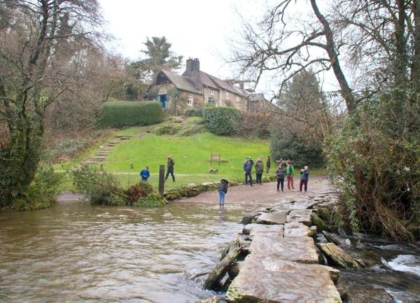 People preparing to cross an ancient clapper bridge over the River Barle at Tarr Steps.