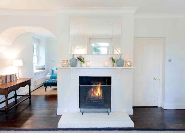 A wood burner beneath a mantlepiece containing candles in glass bowls