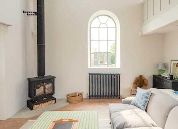 Lounge area with an arched widow,  a sofa, sideboard and wood burner.