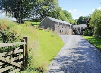 A drive flanked by lawns to an Exmoor barn conversion overlooked by beech trees.