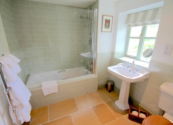 A fully-tiled bathroom with a bath with an overhead shower, WC, washbasin and heated towel rails.