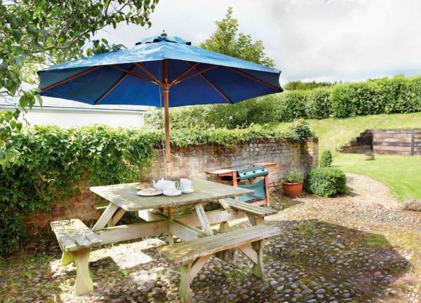 A cobbled courtyard with a BBQ and a 4-sided picnic table with a parasol.