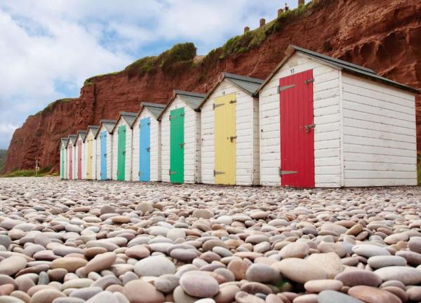 A row of colourful Sidmouth beach huts on a pebble beach beneath a small Devonian sandstone cliff.