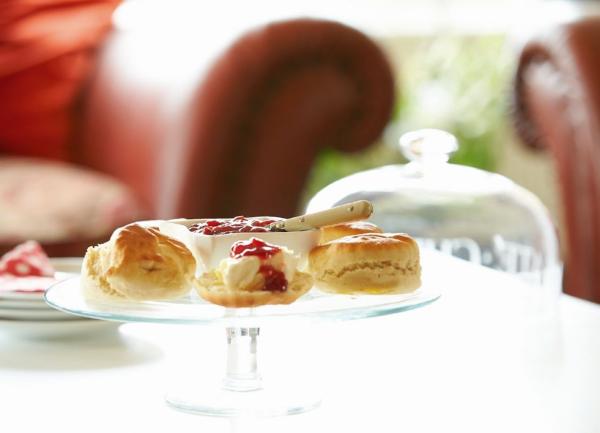 A cake plate on a table piled with scones heaped with layers of cream and jam.