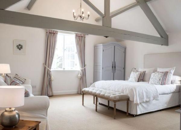 A spacious oak-beamed double bedroom with a bed, wardrobe and large sofa.