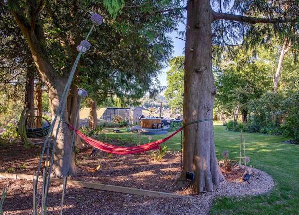 A garden with a hammock tied between two trees, a lawn and a hot tub.