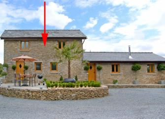 A stone-built Wye Valley holiday cottage overlooks a paved patio with dining furniture.