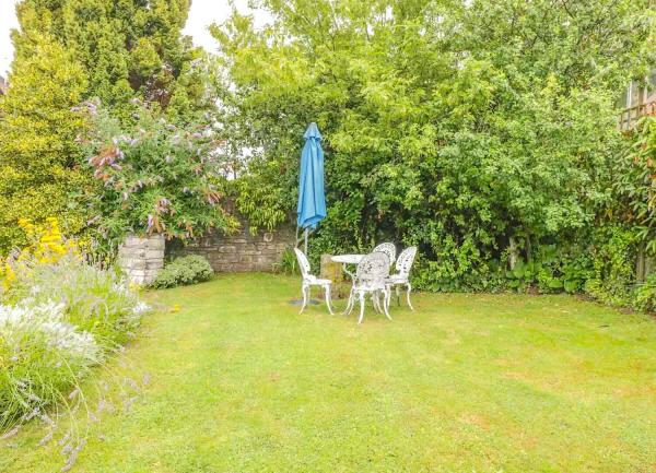 A tea table with a parasol and chairs at the bottom of a lawn by an overgrown stone wall.