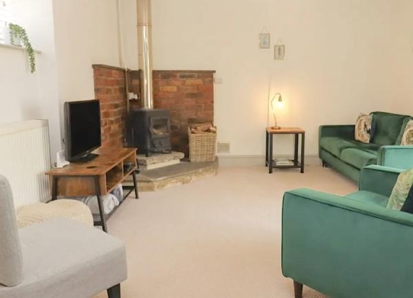 A lounge with a wood burner, TV, a 3-piece suite, additonal armchair and a coffee table with a lamp.
