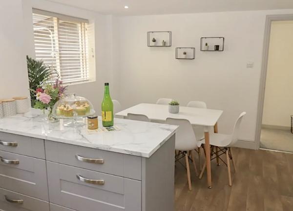 A dining table seating 4 stands beyond a set of kitchen units on a parquet floor.