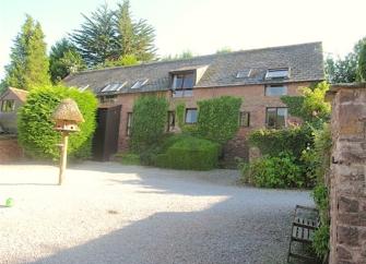 Exterior of a 2-storey Somerset barn conversion overlookig a large courtyard with trees on its edges.