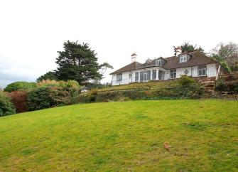 A large rural bungalow with a conservatory overlooks a sloping grassy field.