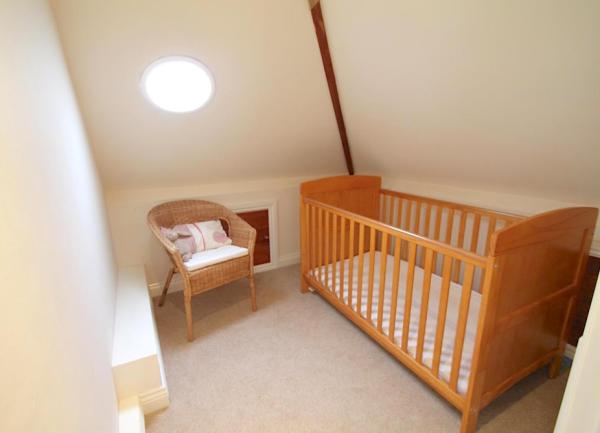 An infant's bedroom with a wooden cost and wicker easy chair.