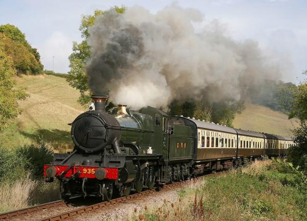A heritage steam engine belching smoke, hauls carriages through the countryside