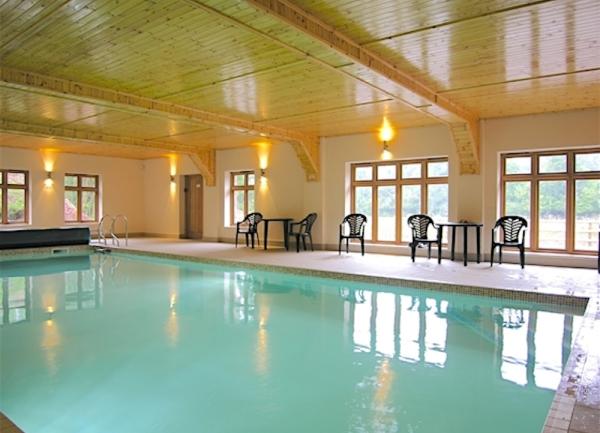 A large indoor heated swimming with patio chairs and tables.
