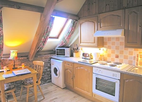 A fitted kitchen with wall and floor cupboards, electric cooker, washing machine, microwave and dining table for two.