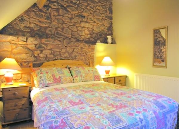 A double bedroom with bed, beside cabinets with table lamps and exposed stone wall.