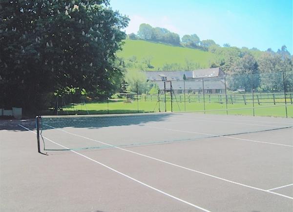 A fenced-in tarmac tennis court with fields and hills beyond.