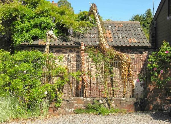 Three life-like, full size Giraffe figures outside a converted barn.