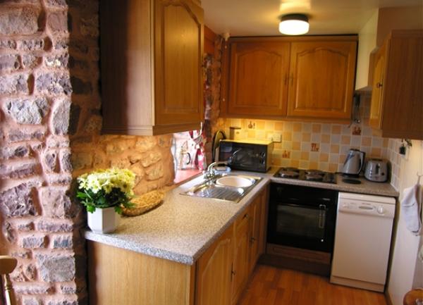 A cosy kitchen with exposed stone walls, oven, dishwasher and microwave.