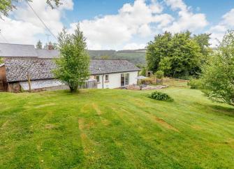 A large lawn slopes down to a large bungalow with Exmoor views beyond.