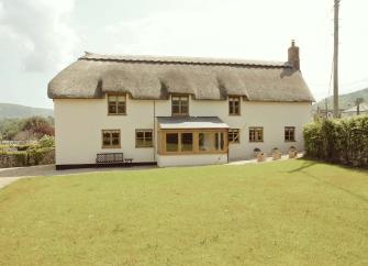 thatched Somerset country cottage overlooks a large lawn.