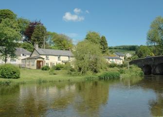 An Exmoor holiday home on the banks of the calm River Barle flowing under a stone bridge.