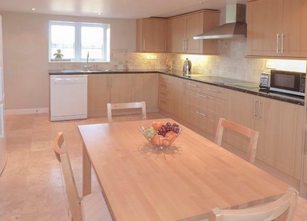 A kitchen with matching floor and wall-mounted cupboards, microwave, dishwasher and dining table.