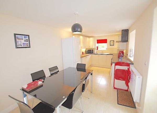 Cottage kitchen with fitted units and wall cupboards and a glass-top dining table and chairs.