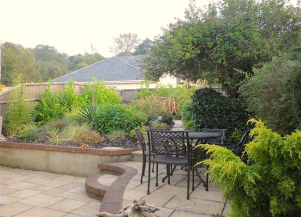 Garden terrace with outdoor dining furniture in a garden filled with shrubs and bushes.