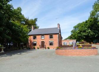 Exterior of a large, double-fronted brick cottage with a spacious parking area and gardens.