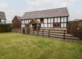 A historic 'black-white white' timbered Herefordshire farm cottage sits behind a terraced and fenced-in lawn.