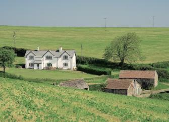 A large North Devon farmhouse and a cluster of three barns, all surrounded by green fields.