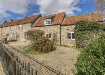 A stone-built exterior of a Dorset cottage with a shingle garden protected by an ornate iron fence.