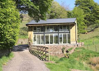 Exterior of a contemporary country cottage with a full-width balcony and floor-to-ceiling bi-fold glass doors.
