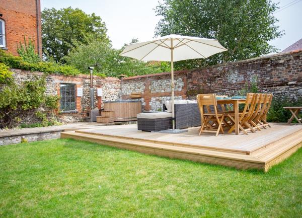 A walled garden with a lawn, dining terrace and hot tub.