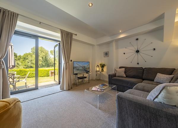 A spacious lounge with sofas, armchair, coffee table, TV and French windows to a large garden.