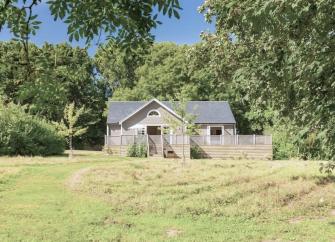 On the edge of a mature wood, a timber-frame lodge with a spacious deck overlooks an open field.