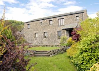 A barn conversion in Kendal overlooks a lawn surrounded by mature shrubs and bushes.