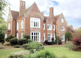 A large rectory and coach house overlook a lawn with a table laid for lunch.