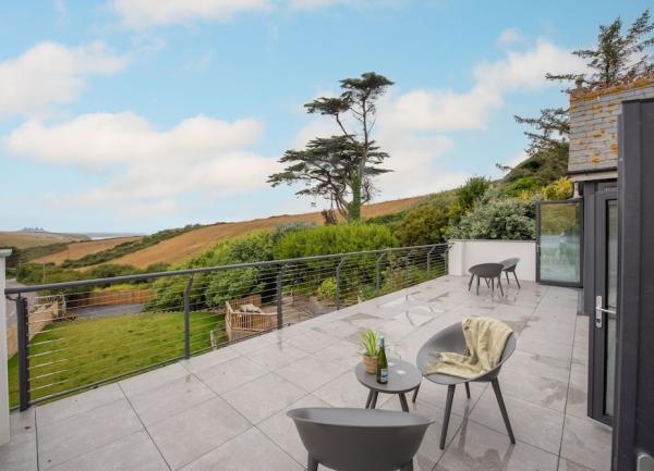 A 1st floor patio overlooks Cornish fields and down to a beach and the sea.