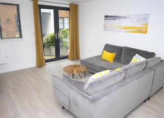 L-shaped sofa with cushions and coffee table in a stylish lounge with French windows to a balcony.