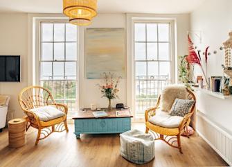 A wood floored lounge with wicker arm chairs and sea views through floor-to-ceiling windiows.