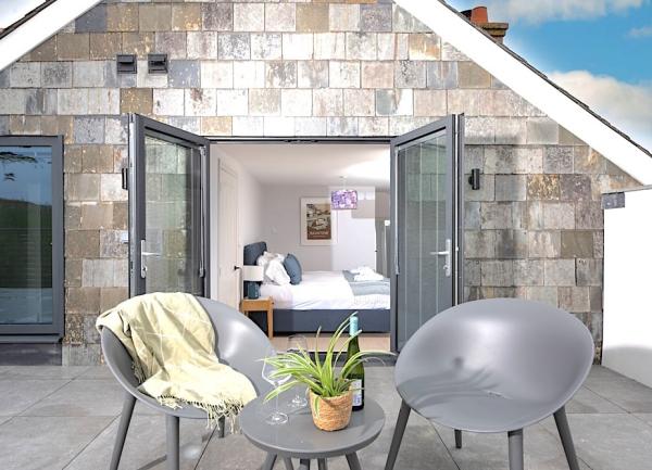 A coffee table and 2 chairs on a terrace with open French windows behind revealing a bedroom.