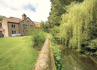 A Norfolk cottage overlooks a spacious lawn and a riverbank with willow trees.